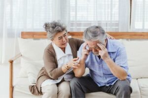 A woman comforts an older man who is experiencing symptoms of dizziness and loss of balance while walking.